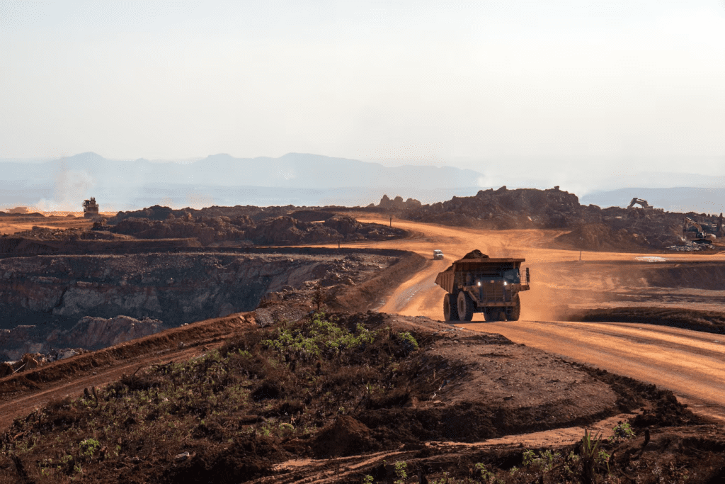 Caminhão de mineração em uma estrada de terra em uma mina a céu aberto, com montanhas ao fundo.