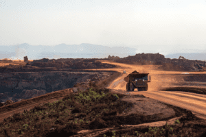 Caminhão de mineração em uma estrada de terra em uma mina a céu aberto, com montanhas ao fundo.