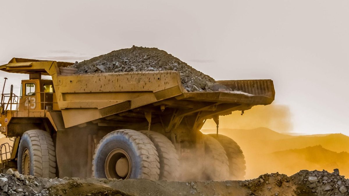 Caminhão de mineração grande carregando areia em um local de mineração ao entardecer.