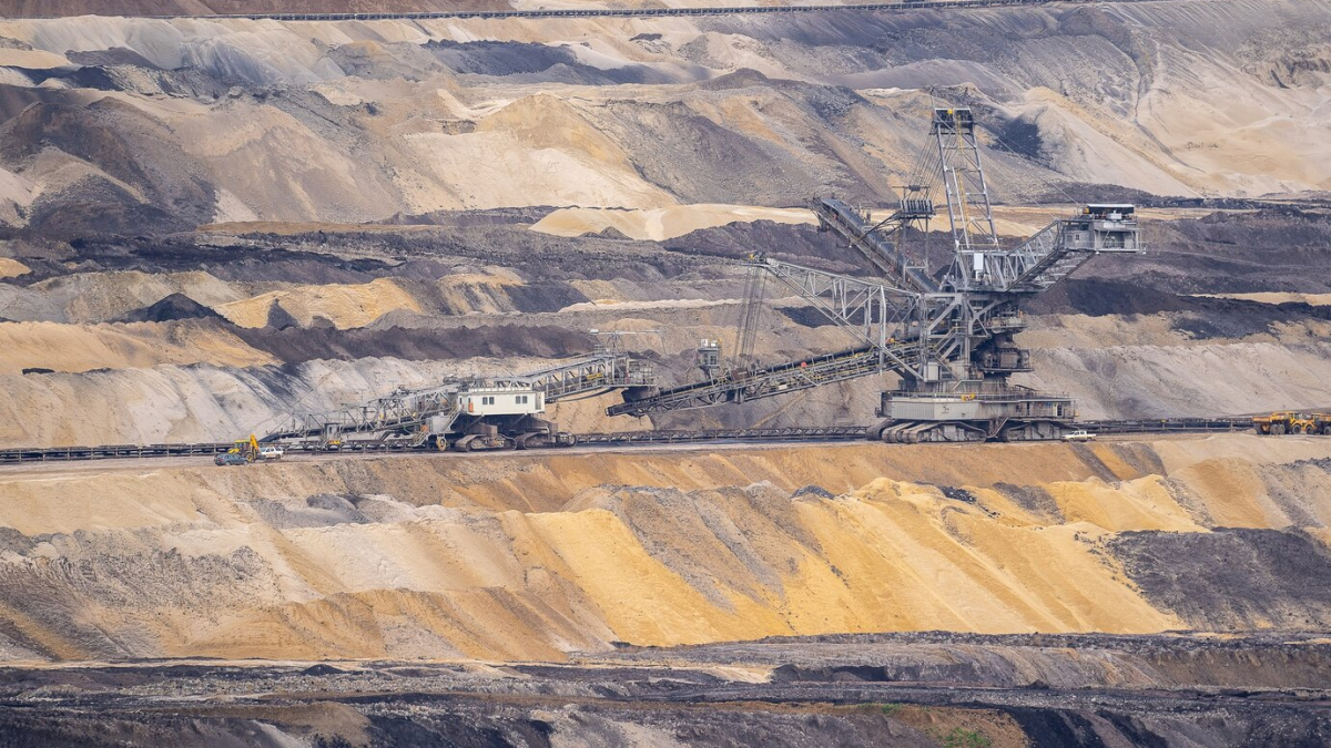 Equipamento de mineração de grande porte em uma mina a céu aberto, com camadas de terra visíveis em diferentes cores.