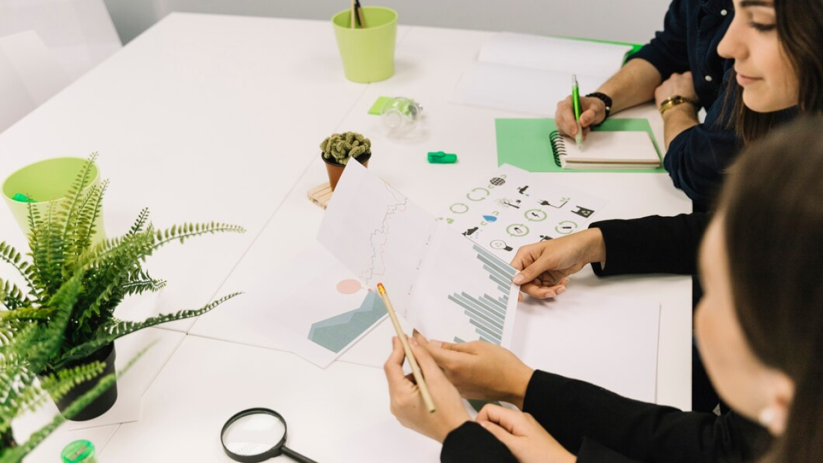 Grupo de pessoas analisando gráficos e dados em um ambiente de trabalho sustentável, com materiais verdes sobre a mesa.