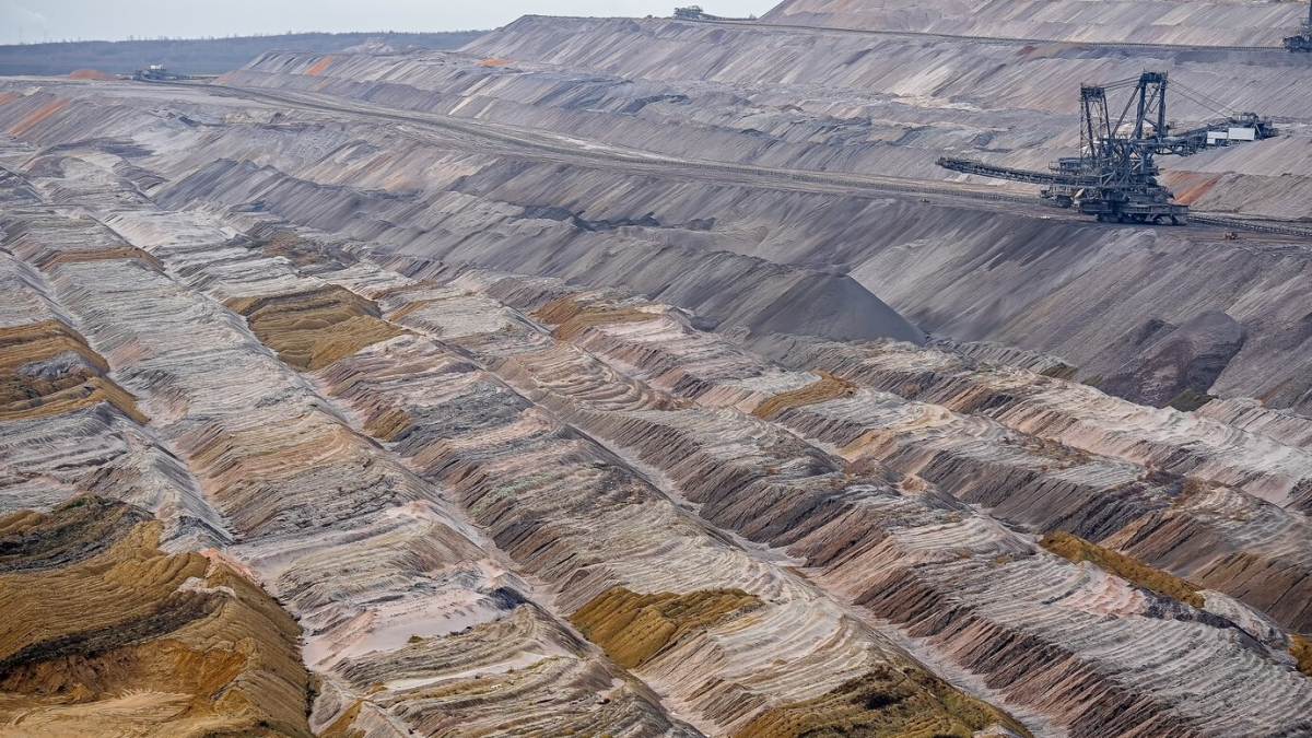 Vista de uma grande mina com camadas de terra escavada e máquinas de mineração.